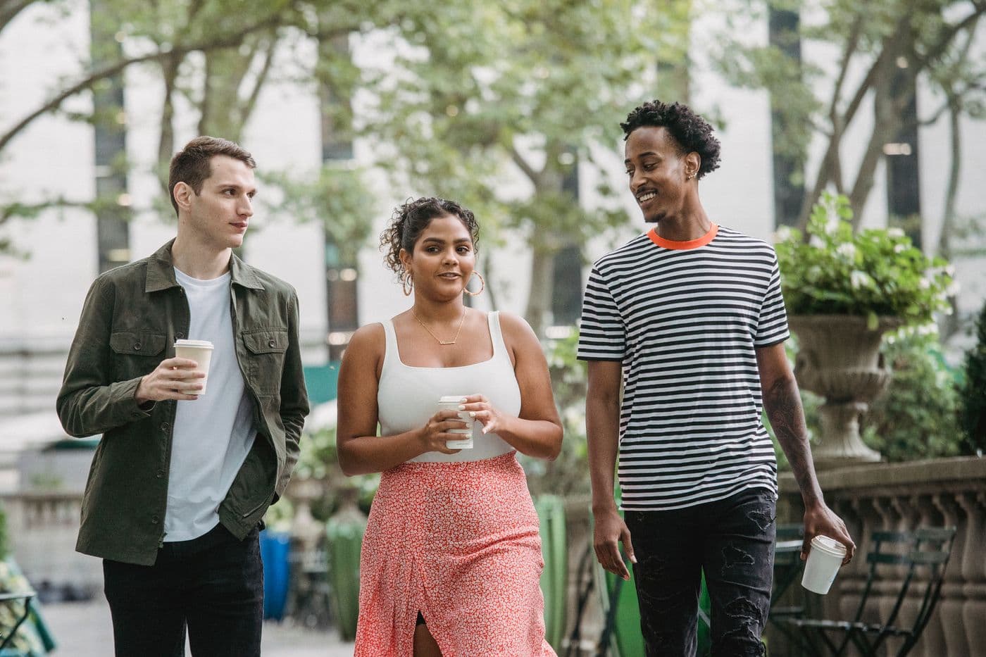 Three friends walking through a city park with takeaway coffee
