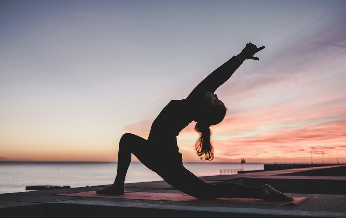 A woman stretching on a waterfront at sunset